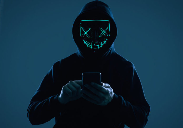 Anonymous Man In A Black Hoodie And Neon Mask Hacking Into A Smartphone