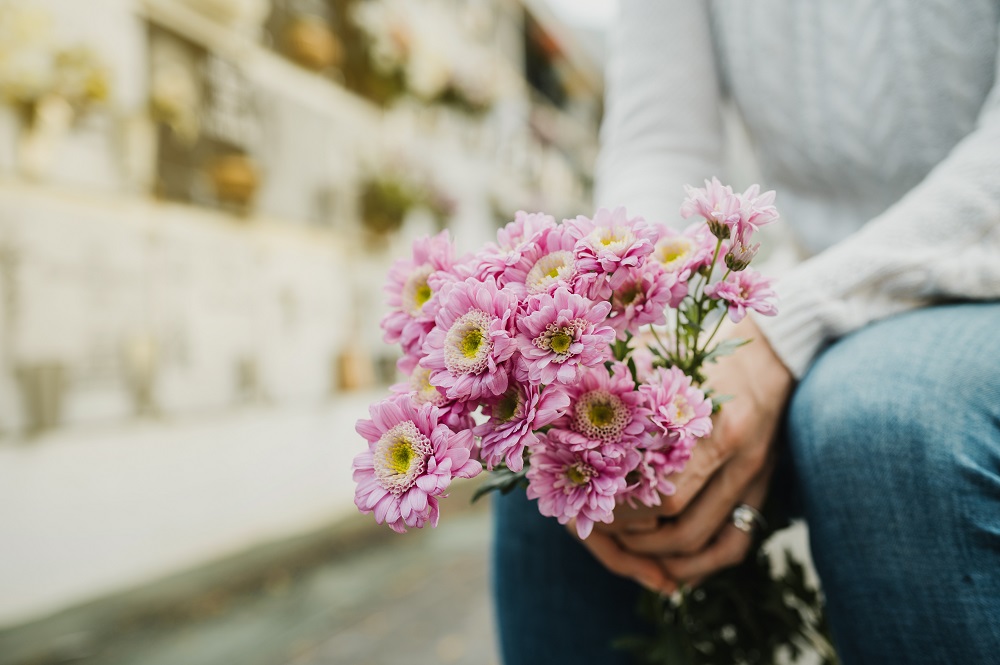 Faceless woman with flowers bouquet in hands sitting in cemetery