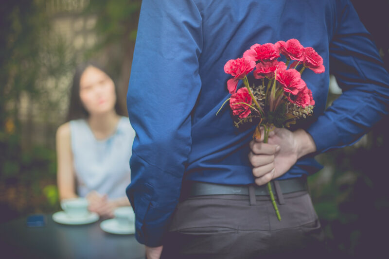 Man Is Hiding Flowers Behind Their Backs To His Girlfriend.